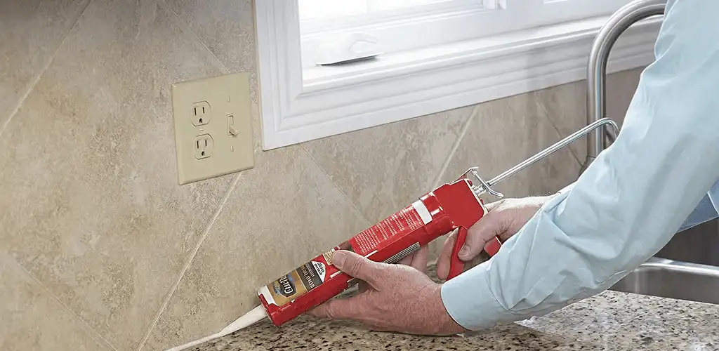 Handyman applying caulk along a kitchen backsplash and countertop seam in Columbus, OH